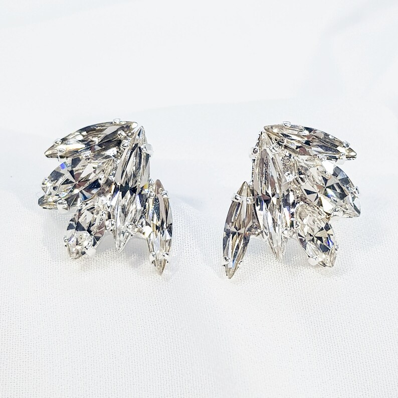 May include: A pair of silver-tone earrings featuring a cluster of clear marquise-shaped crystals. The crystals are arranged in a fan shape.