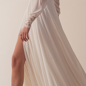 May include: A white flowing gown with a lace trim on the sleeves. The gown has a slit up the side and is made of a soft, flowing fabric.