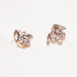 May include: A pair of gold earrings featuring clear crystal marquise-shaped stones. The stones are clustered together, creating a delicate and elegant design.