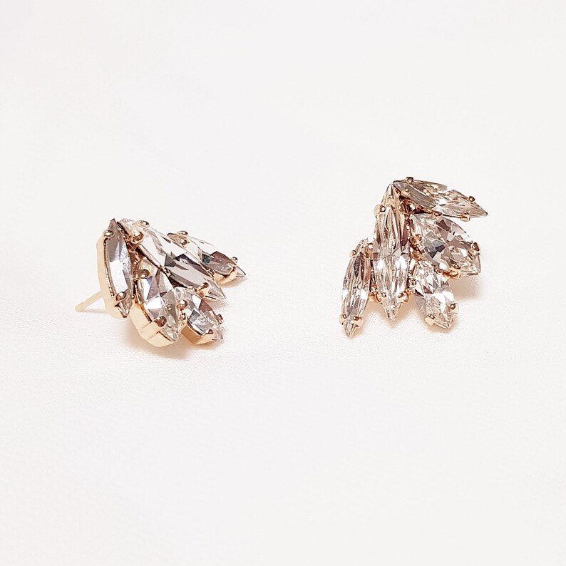 May include: A pair of gold earrings featuring clear crystal marquise-shaped stones. The stones are clustered together, creating a delicate and elegant design.