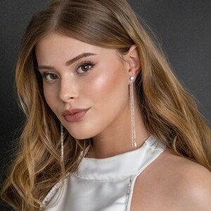 May include: A woman wearing a white halter top with long, silver dangle earrings. The earrings have multiple strands of small, clear crystals.