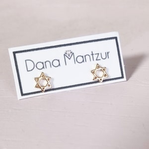 May include: Gold Star of David earrings on a white card with the text "Dana Mantzur" printed on it.