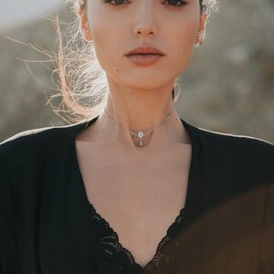 May include: A woman wearing a black top with a delicate silver choker necklace featuring a small flower pendant.