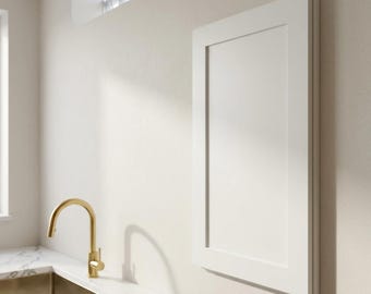 May include: A rectangular white cabinet door with a flat centre panel and a raised frame border, mounted vertically on a wall. Beside it is a stainless steel sink basin with a curved gold tap set into a white marble countertop with grey veining.