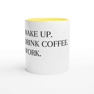 Könnte beinhalten: Weiße Keramik-Kaffeetasse mit gelbem Innenraum. Der Becher hat den Text "WAKE UP. DRINK COFFEE. WORK." in Schwarz aufgedruckt. Eine Standardgröße für Kaffee oder Tee.