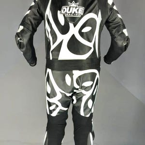 May include: Black and white motorcycle racing suit with white abstract designs. The suit has the text "DUKE RACING" on the chest. The suit has protective padding on the shoulders and knees.
