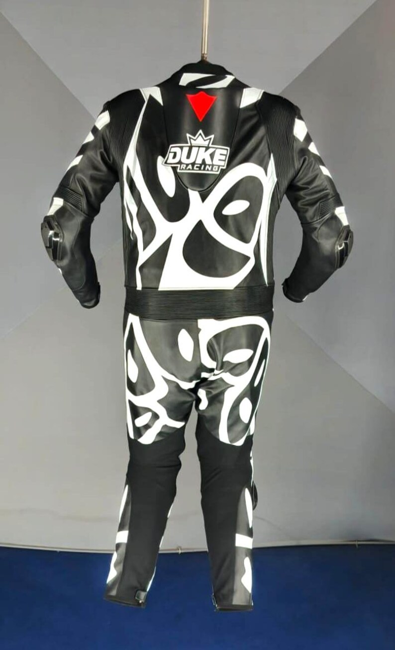 May include: Black and white motorcycle racing suit with white abstract designs. The suit has the text "DUKE RACING" on the chest. The suit has protective padding on the shoulders and knees.