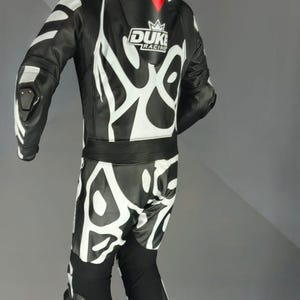May include: Black and white motorcycle racing suit with an abstract pattern. The suit has the "DUKE RACING" logo and a red accent. Includes protective padding on the shoulders, elbows, and knees.
