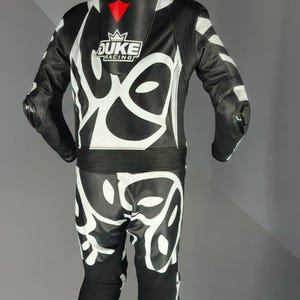 May include: Black and white motorcycle racing suit with a striking graphic pattern. The suit displays the "DUKE RACING" logo in white with red details. Designed for safety and performance on the track.