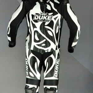 May include: Black and white motorcycle racing suit with the "DUKE RACING" logo. The suit features a striking design with white patterns on a black background. Includes knee pads and shoulder protection.