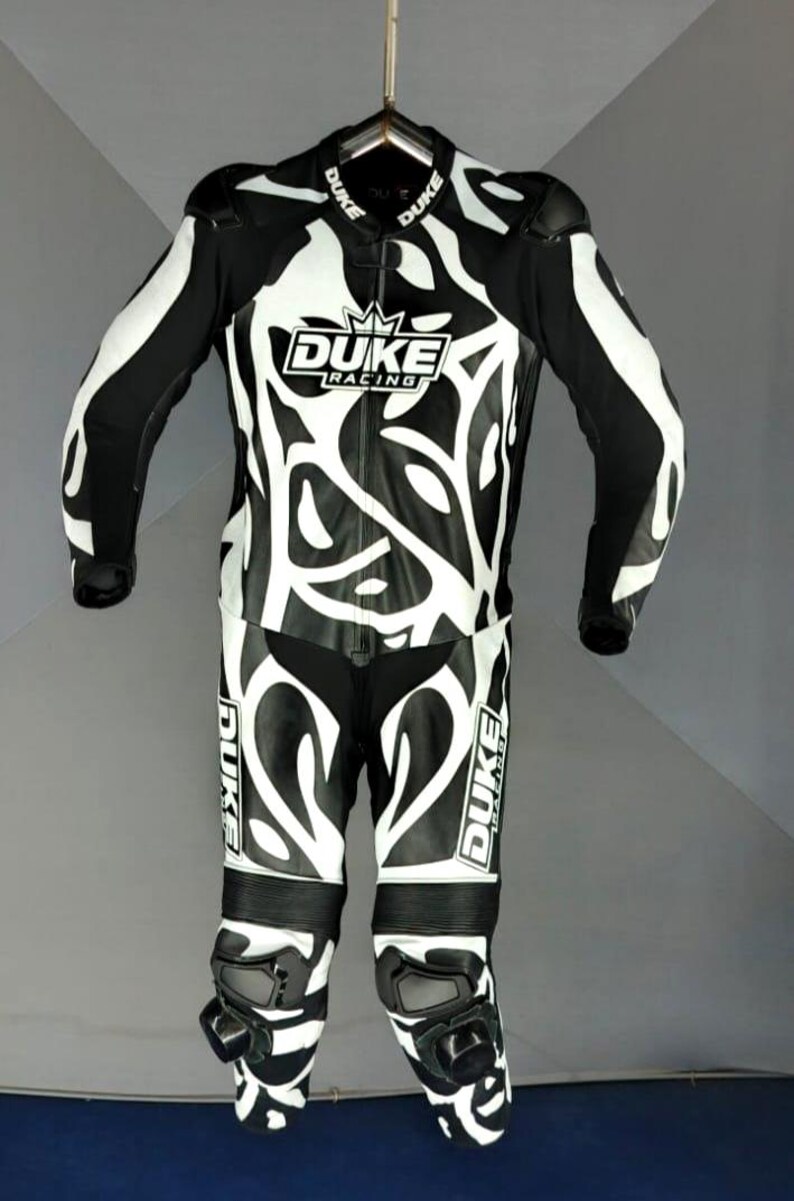 May include: Black and white motorcycle racing suit with the "DUKE RACING" logo. The suit features a striking design with white patterns on a black background. Includes knee pads and shoulder protection.