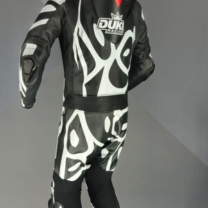 May include: Black and white motorcycle racing suit with the text "DUKE RACING". The suit features white abstract designs. The suit is suspended from a hanger.