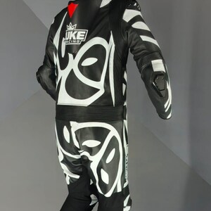 May include: Black and white motorcycle racing suit with a striking graphic pattern. The suit displays the "JUKE RACING" logo and red detailing. Constructed from leather, it includes protective padding on the shoulders, elbows, and knees.