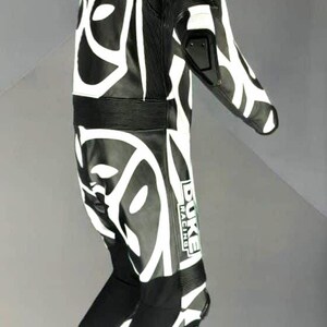 May include: Black and white motorcycle racing suit with a striking abstract pattern. The suit displays the "DUKE RACING" logo and protective padding. The suit is suspended from a hanger.