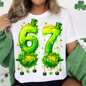 Peut inclure: T-shirt blanc avec un motif de la Saint-Patrick représentant le chiffre 67 en vert dégoulinant, un chapeau de leprechaun et des pièces d'or. Le motif comprend des trèfles et des chaudrons d'or.