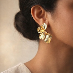 Peut inclure: Boucles d'oreilles florales dorées. Les boucles d'oreilles sont conçues pour ressembler à une fleur avec de multiples pétales texturés. Les boucles d'oreilles sont portées sur l'oreille et sont de couleur or vif et brillant. Les boucles d'oreilles sont une pièce maîtresse.