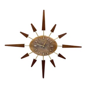 Puede incluir: Un reloj de pared moderno de mediados de siglo con un diseño de estrella. El reloj presenta una esfera ovalada de color marrón claro con manecillas y marcadores dorados. Los detalles de madera marrón oscuro irradian desde el centro.