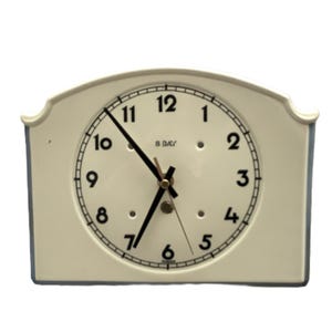 May include: Cream-coloured, rectangular clock with a white face and black numerals. The clock hands are black, and the face reads "8 DAY". The clock has a curved top and a classic design. A vintage-style timepiece.