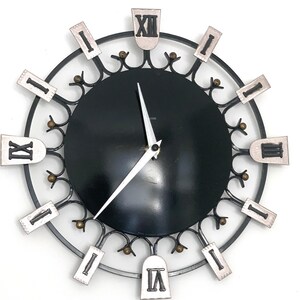 May include: A black and silver wall clock with Roman numerals. The clock face is black, surrounded by a silver metal frame with decorative accents. The hands are white, and the numerals are in a rectangular shape.