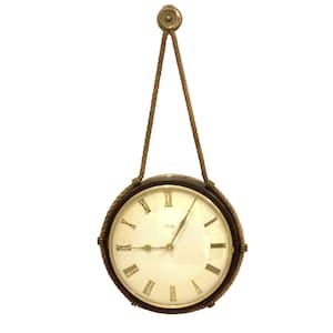 May include: A round wall clock with a dark brown frame and a cream-coloured face featuring black Roman numerals. The clock is suspended by a braided gold-toned rope that attaches to a circular brass wall mount at the top, with gold-toned clock hands.