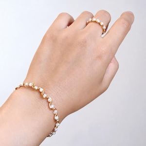 May include: A gold-toned wire bracelet and a matching gold-toned wire ring, both featuring a continuous, undulating wave design set with small, round, white pearls spaced evenly along the length of the metal wire structure.