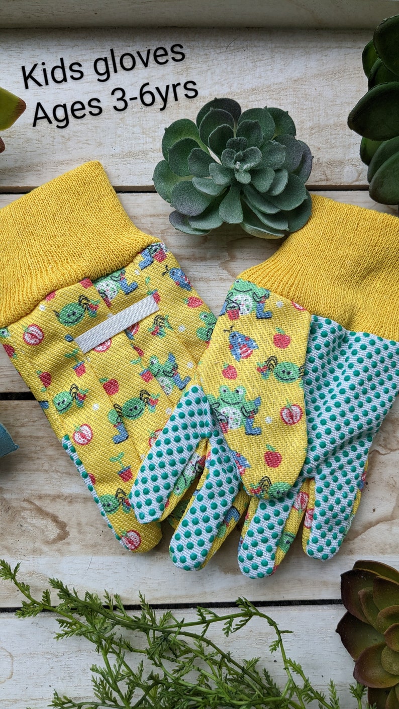 May include: A pair of yellow gardening gloves with a green and white polka dot pattern on the fingertips. The gloves have a cartoon print of green bugs and red apples. The gloves are labeled "Kids gloves Ages 3-6yrs".