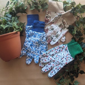 May include: Four pairs of gardening gloves with floral patterns. Two pairs are blue and white with small floral designs, one pair is white with red and blue flowers, and one pair is white with brown and pink flowers.