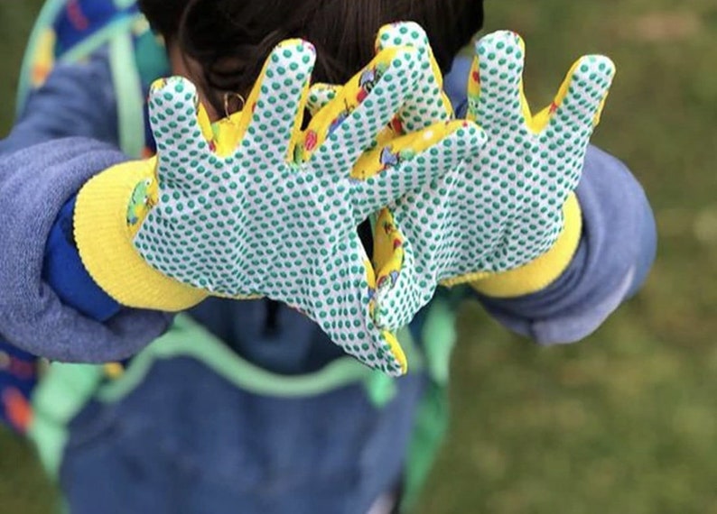 May include: A pair of yellow gardening gloves with a green and white polka dot pattern and colorful cartoon images. The gloves have a textured grip.