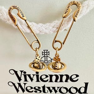 Peut inclure: Une paire de boucles d'oreilles épingle à nourrice dorées avec une breloque logo orbe Vivienne Westwood. Chaque épingle est gravée du texte Vivienne Westwood sur la courbe supérieure. Les boucles d'oreilles sont présentées sur une carte avec le texte Vivienne Westwood Jewellery.