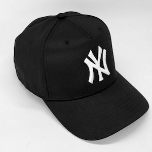 Può includere: Cappellino da baseball nero con logo "NY" bianco ricamato sul davanti. Il cappellino ha una visiera curva e una corona strutturata. Il cappello è realizzato in un tessuto resistente ed è adatto all'uso quotidiano.