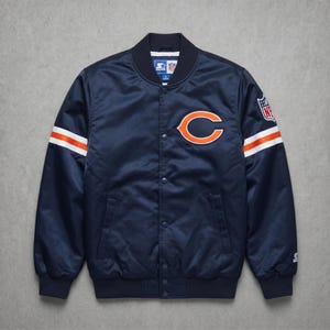 Peut inclure: Veste de bombardier bleu marine des Bears de Chicago. Comprend le logo orange et blanc de l'équipe sur la poitrine et les manches. Comprend l'écusson du logo NFL. La veste a une fermeture à boutons-pression et un col et des poignets côtelés.