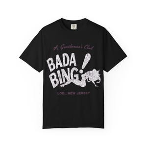 May include: Black t-shirt featuring the text "A Gentleman's Club" above "BADA BING!" and an illustration of a woman. The text "Lodi, New Jersey" is below the illustration.