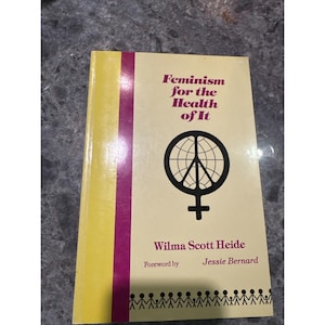 May include: A book titled "Feminism for the Health of It" by Wilma Scott Heide. The cover is cream-colored with a purple stripe and a graphic of a peace sign inside a globe and a female symbol. The book has a yellow spine.