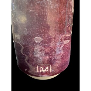 May include: A handmade ceramic mug with a deep burgundy glaze. The mug has a cylindrical shape with a slightly textured surface and a white base. The bottom of the mug features a stamped logo. The mug is suitable for hot or cold beverages.