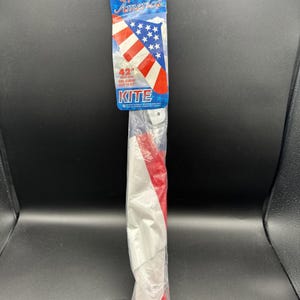 May include: A 42-inch wing span kite packaged in a clear plastic sleeve. The header card features a red, white, and blue American flag design with the text "Great America" and "KITE". The kite material inside is also red, white, and blue.