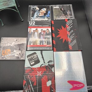 Könnte beinhalten: Eine Sammlung von U2-Musikmedien, bestehend aus zwei Elevation Tour-CDs, der DVD An Unforgettable Journey, einem How to Dismantle an Atomic Bomb-Sonderedition-Boxset, einer Go Home Live from Slane Castle-CD, einer U2 Live Boston-DVD und einem Pop-Album.