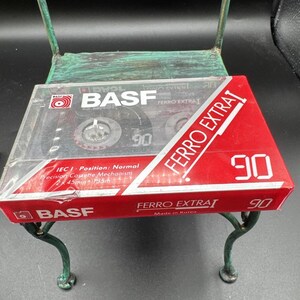 May include: A BASF Ferro Extra I 90-minute audio cassette tape in its original clear plastic case. The packaging features a red and white design with the text BASF, Ferro Extra I, and 90 prominently displayed. It indicates IEC I Normal position.