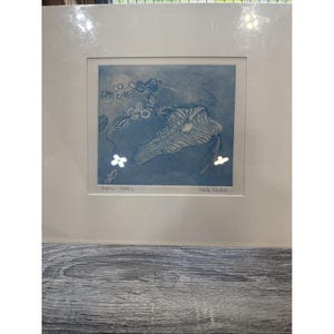 May include: A blue and white print of an abstract design, framed in a white mat. The print features organic shapes and floral elements. The artist's signature is visible in the lower right corner. The title "Futilia - Futil" is printed in the lower left corner.