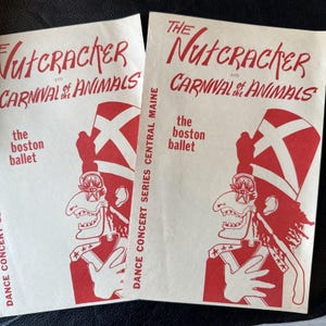 Może przedstawiać: Dwa zabytkowe programy wydarzeń dla "Dziadka do Orzechów i Karnawału Zwierząt" w wykonaniu Boston Ballet. Programy są wydrukowane czerwonym tuszem na kremowym papierze. Okładka przedstawia żołnierza z dużym kapeluszem i flagą.