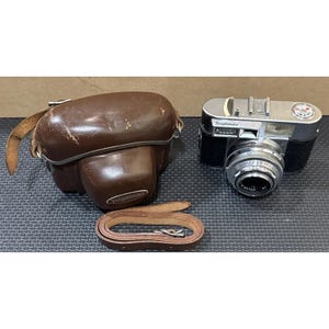 May include: A vintage silver and black Voigtlander camera with a lens, brown leather case, and a brown leather strap. The camera has a silver lens and a black body. The case is brown and has the Voigtlander logo.