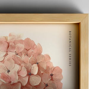 May include: A framed botanical print featuring a close-up of pink hydrangea flowers. The artwork is part of the "Botanical Series" and is set within a light wood frame, creating a natural and elegant aesthetic.
