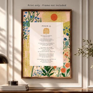 Peut inclure: Une affiche murale rectangulaire présentant le texte du Psaume 23 au centre avec une icône d'arbre doré au-dessus. La bordure affiche une illustration colorée de fleurs sauvages, de blé et d'un soleil sur fond rose pâle. Texte : Print only.