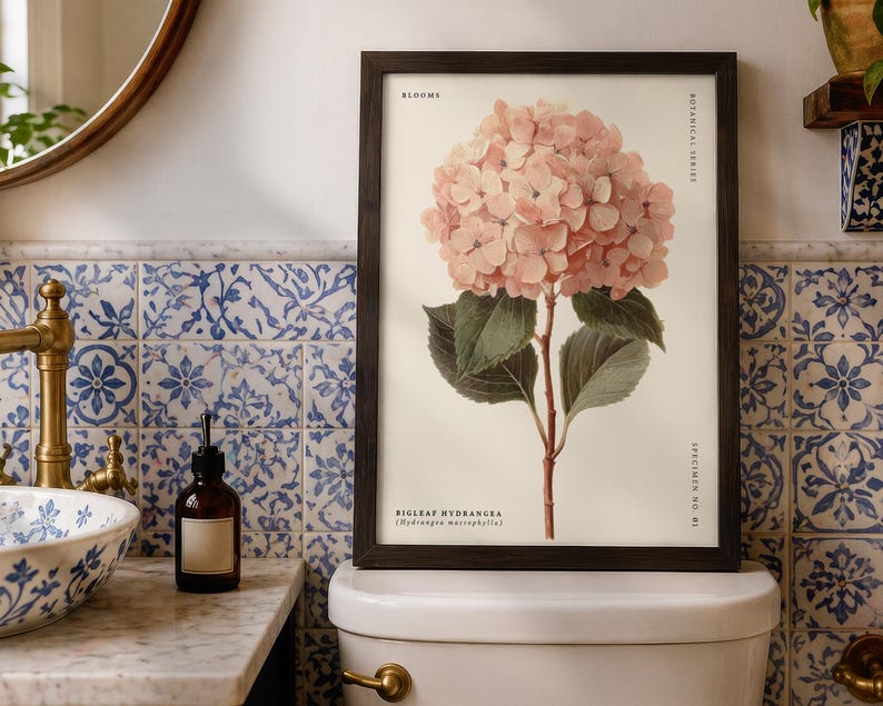 May include: A framed botanical print of a pink bigleaf hydrangea flower. The print is labeled "Blooms" and "Botanical Series" with the scientific name. The print is displayed in a bathroom with blue and white tile.