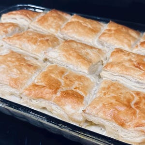 May include: A rectangular glass baking dish filled with golden-brown, square pastries. The pastries have a flaky, layered texture and are baked to a light, crispy finish. The dish appears to contain a creamy filling, suggesting a savory or sweet dish.