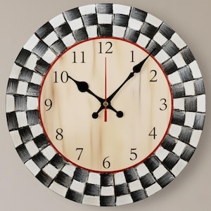 Puede incluir: Reloj de pared redondo con esfera color crema y números negros. El reloj tiene manecillas negras y un segundero rojo. El borde exterior presenta un patrón de cuadros blancos y negros, y el diámetro del reloj es de unos 30 cm.