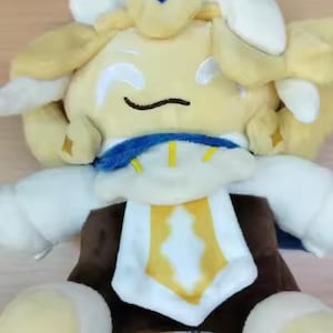 May include: A plush toy character with a yellow head, white arms, and a brown torso. The character has a blue collar and a yellow and white emblem on its chest. The toy is sitting on a wooden surface.