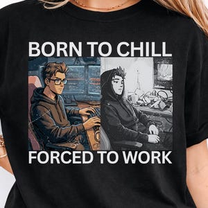 Puede incluir: Camiseta negra con el texto "BORN TO CHILL FORCED TO WORK" sobre un gráfico de dos personas frente a computadoras. Una persona usa gafas y la otra una sudadera con capucha. La camiseta es de estilo casual.