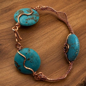 May include: A handcrafted copper bracelet featuring three turquoise stones. The stones are a vibrant blue-green color with brown marbling. The copper wire is intricately woven and shaped, creating a unique and artistic design. The bracelet is a piece of jewelry.
