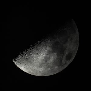 May include: A close-up image of the moon in its crescent phase, set against a black background. The moon's surface is textured with craters and varying shades of gray, with the illuminated portion sharply defined.