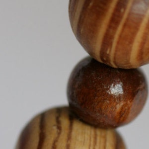 May include: A close-up of a wooden bead necklace with brown and light brown striped beads. The beads are round and have a smooth finish.